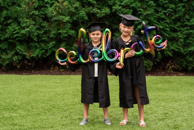 Kinder in Absolventenkleidung mit celebrate Ballon