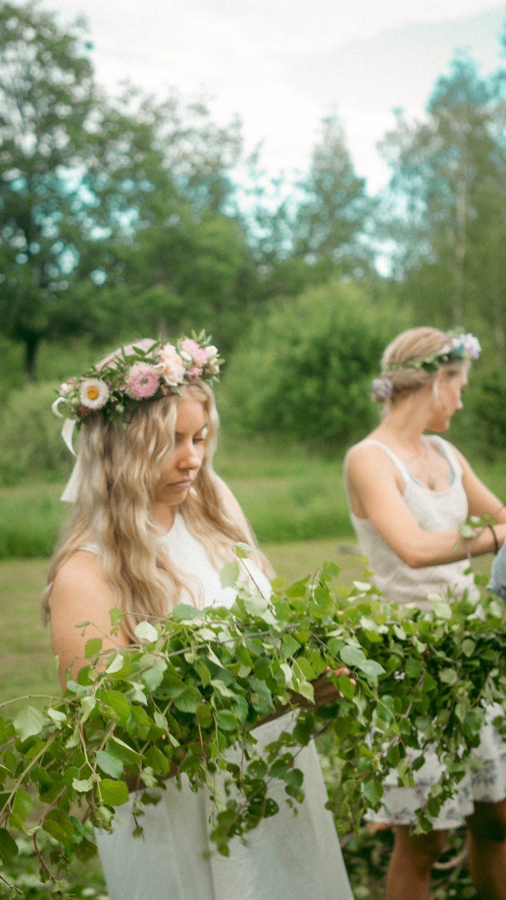 Zwei Frauen mit Blumenkranz binden Mittsommerbaum